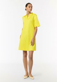 Gelbes Kurzarmkleid mit Polokragen, aus glattem Stoff gefertigt, hat einen geraden Schnitt und endet oberhalb des Knies.