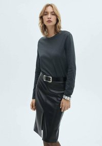 Haut à manches longues gris foncé associé à une jupe crayon en cuir noir avec une fente sur le devant, une large ceinture à boucle en argent et un bracelet texturé.