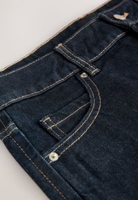 Jeans in denim blu scuro con un design strutturato, cuciture beige a contrasto, una tasca frontale e una chiusura con bottone argentato.