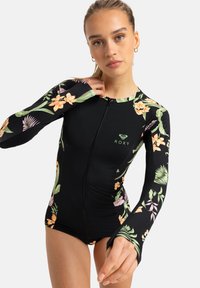 Maillot de bain noir à manches longues avec des motifs floraux dans des teintes d'orange et de vert. Il dispose d'une fermeture éclair sur le devant et d'un design ajusté de Roxy.