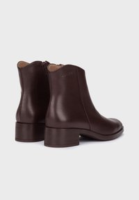 Botas de cuero marrón hasta el tobillo con una textura suave, tacón bajo y cierre con cremallera en la parte trasera. Diseño limpio y aerodinámico con un mínimo de marcas.