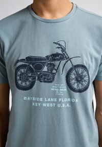 Modrá bavlněná tričko s grafikou motocyklu v tmavě modré barvě a textem pod ním včetně "BAYSIDE LANE FLORIDA KEY WEST U.S.A."