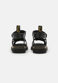 Black sandals with a textured leather finish, featuring open backs, adjustable straps, and contrasting yellow stitching along the soles.