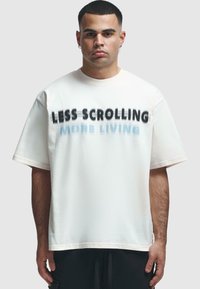 T-shirt en coton blanc à manches courtes, avec un texte noir en gras "MOINS DE DÉFILEMENT" et un " PLUS DE VIE " bleu clair sur le devant.