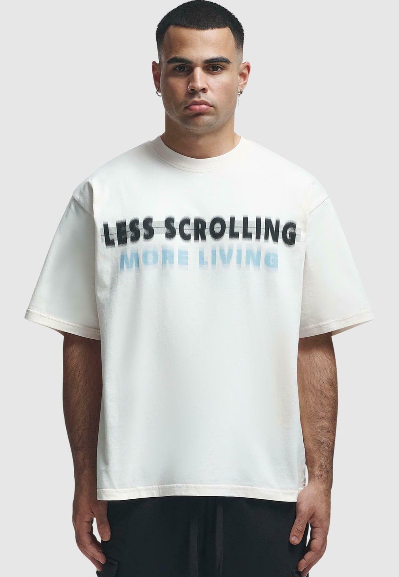 Hvid bomulds t-shirt med korte ærmer, der har fed sort tekst "LESS SCROLLING" og lysere blå "MORE LIVING" på fronten.