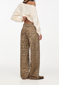 Pantalon à jambes larges imprimé léopard en marron et beige, fabriqué en tissu doux, avec une taille haute et des poches arrière. Conception légère et fluide.