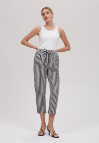 Un débardeur blanc à côtes associé à un pantalon taille haute rayé en bleu marine et blanc, avec un devant noué et une longueur crop. Sandales noires à talons.