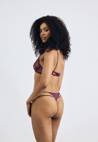 Ensemble de lingerie en dentelle violette comprenant un bralette avec des panneaux transparents et des bretelles ajustables, accompagné d'un string assorti avec des détails délicats.