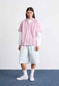 Chemise courte rose à manches courtes, chemise à manches longues de couleur claire en dessous, short léger bleu clair ample, chaussettes blanches mi-mollet, et baskets lavande.