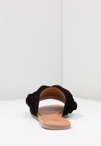 Svarta mocka slide-sandaler med öppen häl, böjd blommig design på remmarna och en platt tanfärgad innersula för komfort.