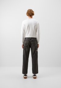 Pantalones cargo de mezclilla gris con un corte relajado, costuras visibles y múltiples bolsillos. Combinados con una camiseta de manga larga blanca.