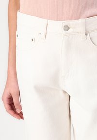 White denim jeans feature a classic five-pocket design, metal hardware, and stitched details, showcasing a smooth, textured finish.