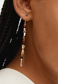 Orecchini in oro con un design unico caratterizzato da accenti metallici sagomati, perline colorate in rosso, nero e grigio, e un elemento lineare pendente.
