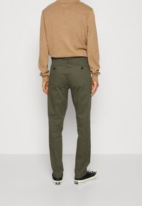 Olivgröna bomullbyxor med rak passform, bakfickor med svarta knappar, kombinerat med en beige tröja och svarta låga sneakers.