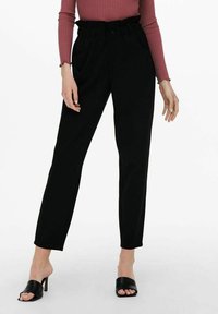 Zwarte high-waisted broeken met een platte voorkant, zijzakken en taps toelopende pijpen, gemaakt van een gladde stof, gecombineerd met zwarte open teen hakken.