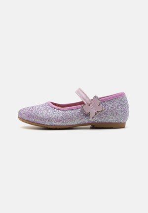 Child’s glittery pink Mary Jane shoe with butterfly-shaped strap fastener and brown flat sole, side view on white background.