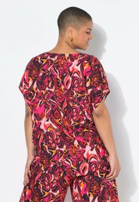 Top multicolore con fantasia astratta a maniche corte, che presenta tonalità di rosa, rosso e nero. Tessuto leggero e vestibilità comoda.