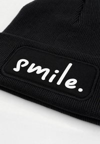 Black beanie hat with ribbed texture, featuring a rectangular black patch with the word "smile." in white, bold lettering.