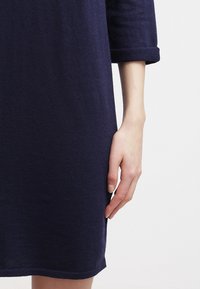 Abito blu navy in tessuto a maglia testurizzata, con maniche a tre quarti arrotolate e taglio dritto. Presenta una vestibilità comoda.