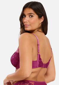 Soutien-gorge en dentelle de couleur magenta profond avec des bretelles réglables, fermeture à crochets et œillets au dos, et motif floral sur les bonnets. Design du dos lisse.