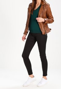Brown leather biker jacket over a green v-neck sweater, paired with black skinny jeans and white sneakers. Smooth textures and fitted design.