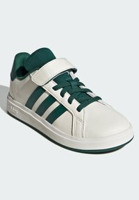 White and dark green Adidas sneaker with velcro strap and laces, three side stripes, and a textured rubber sole.