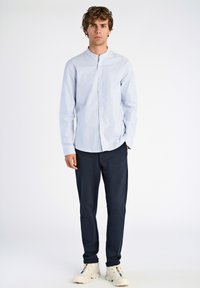 Camicia a righe blu chiaro e bianca con colletto alla mandarina, abbinata a pantaloni blu navy e sneakers bianche. Tessuto di trama liscia.
