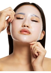 Masque facial en feuille transparent partiellement retiré du visage, mettant en avant une peau lisse et des lèvres d'un ton neutre et uniforme, les mains tenant le masque.