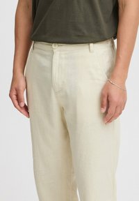 Beige linbukser med rett snitt og frontlommer. Har knapplukking og subtil tekstur. Brukt sammen med en mørkegrønn skjorte.