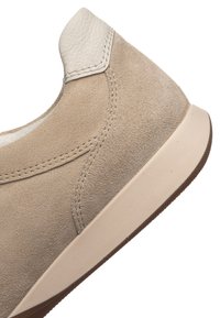 Béžová semišová teniska s bělavým koženým jazykem na patě, detailním prošíváním a světle krémovou gumovou podrážkou s hnědým vzorkem.