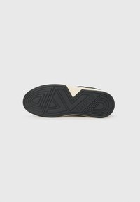 Black rubber sneaker sole with a textured pattern, featuring the brand name "GUESS" embossed on the side in an off-white color.