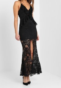 Vestido maxi de encaje negro con un corsé con volantes, escote en V y una abertura alta en el muslo; silueta ajustada con dobladillo acampanado.