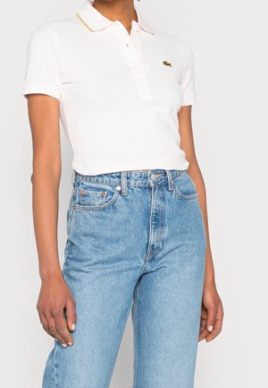 Witte polo met korte mouwen, gouden kraagaccenten en geborduurd logo, gecombineerd met lichtblauwe spijkerbroek met hoge taille.