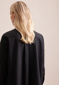 Schwarzes Shirt mit glatter Textur, mit einem strukturierten Kragen, lockerer Passform und einem gefältelten Rücken, von hinten betrachtet.