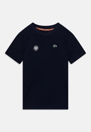 T-shirt à manches courtes bleu marine en coton, arborant un petit logo de crocodile vert et un emblème blanc de Roland Garros sur la poitrine.