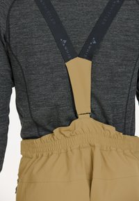 Beige sneeuwbroeken met elastische tailleband en verstelbare zwarte banden. De stof heeft een gladde textuur, geschikt voor wintersport of activiteiten.