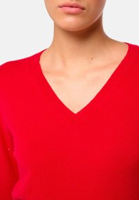 Pull en V rouge en tricot doux. Doté d'un col ribba et d'une coupe ajustée, mettant en valeur la texture lisse et la couleur vive.