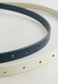 Deux ceintures en cuir fines, une noire et une blanche, chacune avec plusieurs trous de réglage, présentées sur une surface blanche.