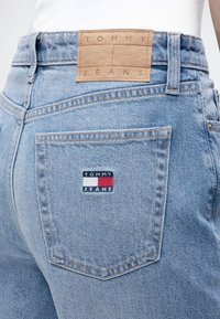 Φωτεινό γαλάζιο τζιν με πίσω τσέπη και δύο λογότυπα Tommy Jeans, ένα δερμάτινο ταμπελάκι στη μέση και ένα ραμμένο στην τσέπη.