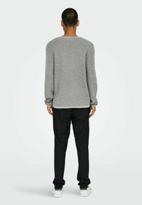 Grauer Strickpullover mit langen Ärmeln und rundem Ausschnitt, kombiniert mit schwarzen Hosen und weißen Sneakers. Einfaches, strukturiertes Design.