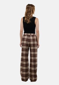 Pantalon à carreaux marron et beige avec une coupe décontractée, doté d'une taille élastique. Assorti avec un haut noir sans manches.