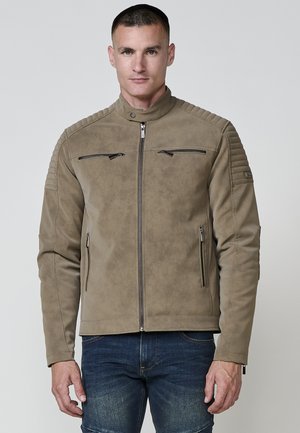 Chaqueta de piel sintética color marrón con acentos de hombros acanalados, dos bolsillos con cremallera y cuello alzado. Textura suave y diseño ajustado.
