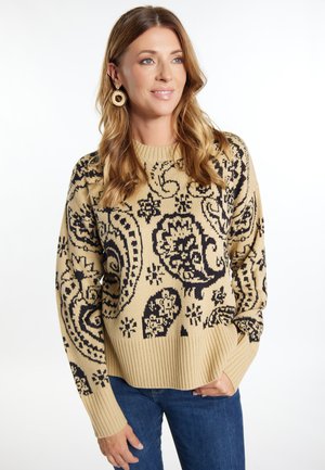 Beige kötött pulóver fekete paisley mintázattal, bordázott mandzsettákkal és szegélyezéssel, sötét farmernadrággal párosítva. Klasszikus kerek nyakkivágással rendelkezik.