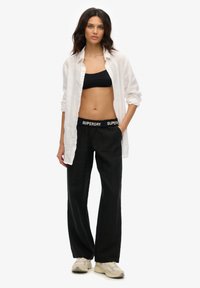 Pantalons en lin noirs avec une taille élastique, associés à un haut noir court et une chemise blanche boutonnée. Les accents comprennent le logo de la marque sur la taille.