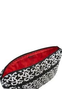 Bolso de patrón blanco y negro con logotipos de "DKNY", con cierre de cremallera y un forro interior rojo. Exterior de tela texturizada.