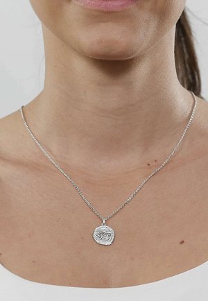 Silver necklace on a thin chain featuring a round pendant with a textured design and detailed engraving, resting on bare skin.