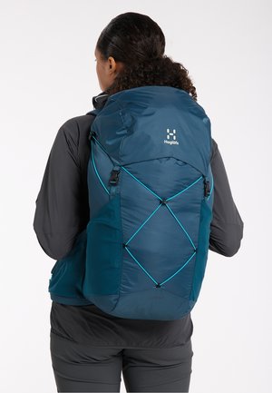 Teal rugzak met een textuurafwerking, voorzien van verstelbare schouderbanden, een trekkoordsluiting en een voorste elastische bungee-systeem voor extra opbergruimte.