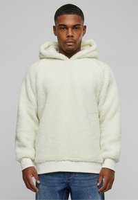 White fleece hoodie with a textured surface, featuring a drawstring hood, ribbed cuffs, and hem. Worn with blue jeans.