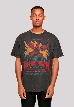 Black oversized t-shirt featuring a vibrant graphic of a Demogorgon, with red and yellow accents, vintage texture, round neckline, short sleeves.
