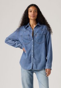 Jasnoniebieska koszula jeansowa z długimi rękawami, z tylnym karczkiem w kształcie litery V, dwoma kieszeniami na piersi i zapięciem na guziki. Miękka faktura i luźny krój.